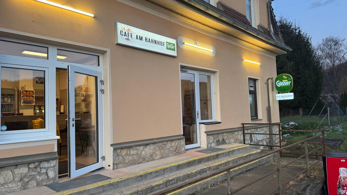 Ein Café mit der Aufschrift „Café am Bahnhof“ an einer Fassade. Der Eingangsbereich hat Stufen und eine einladende Umgebung. | © SV Hinterberg