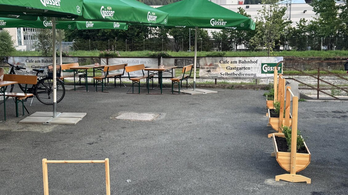Ein gemütlicher Außenbereich mit Holztischen und grünen Sonnenschirmen. Blumentöpfe aus Holz stehen entlang des Platzes. | © SV Hinterberg