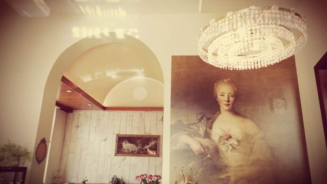 Ein elegantes Café mit einer schönen Wandmalerei einer Dame und einem großen Kronleuchter. Die gesamte Atmosphäre ist gemütlich und einladend. | © Anton Brandner