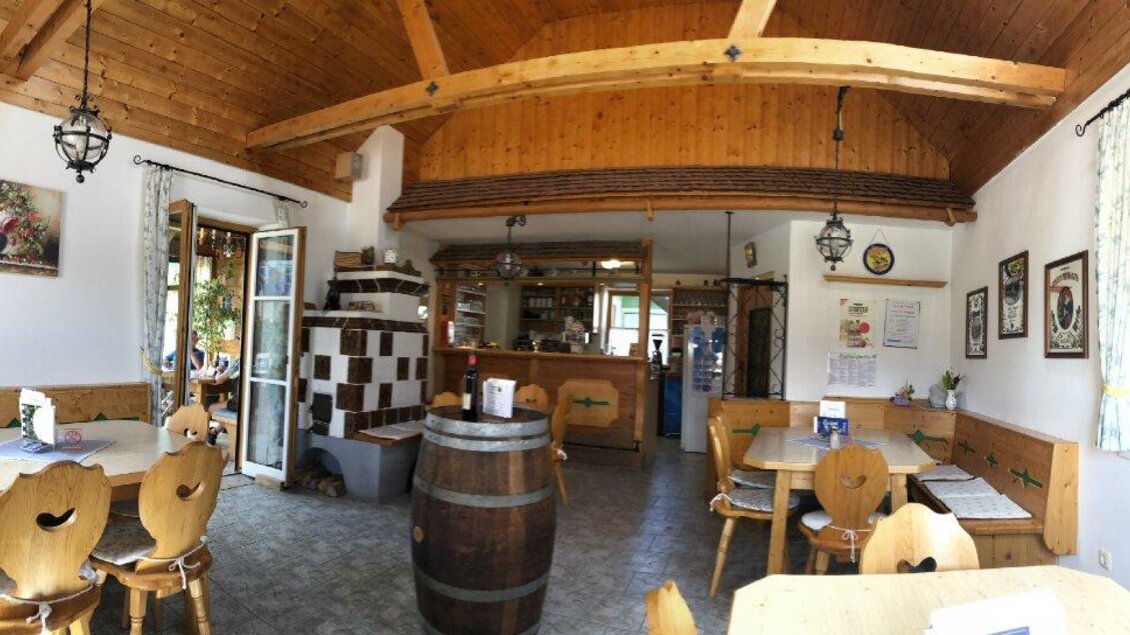 Eine gemütliche Gaststube mit Holzverkleidung und rustikalen Tischen. Der Raum wirkt einladend und hat eine offene Bar im Hintergrund.