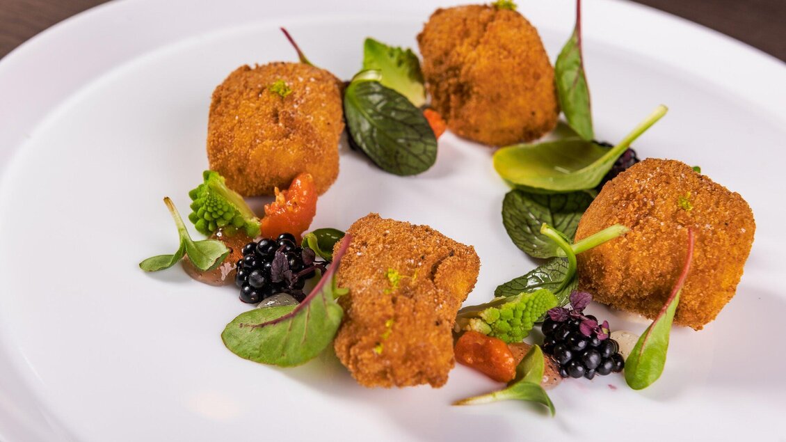 Ein Teller mit knusprigen, goldbraunen Snacks, garniert mit frischen Blättern und bunten Saucen. Die ansprechende Präsentation hebt die Aromen und Texturen hervor. | © Casa Costiera