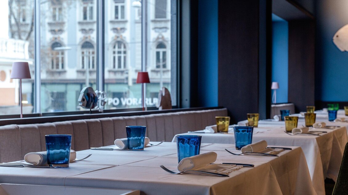 Ein elegantes Restaurant mit gedeckten Tischen und bunten Gläsern. Der Blick zeigt eine Fensteransicht auf eine belebte Straße. | © Casa Costiera