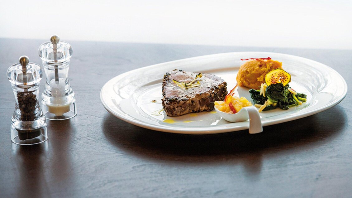 Ein elegant angerichtetes Gericht auf einem weißen Teller. Es besteht aus einem Stück Fleisch, Beilagen und Gewürzmühlen. | © Caylend - Michael Fiedler