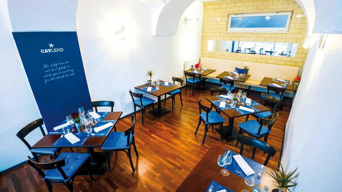 Ein modernes Restaurant mit hellen Wänden und einem eleganten Holzfußboden. Die Tische sind schön gedeckt und laden zum Essen ein. | © Caylend - Michael Fiedler