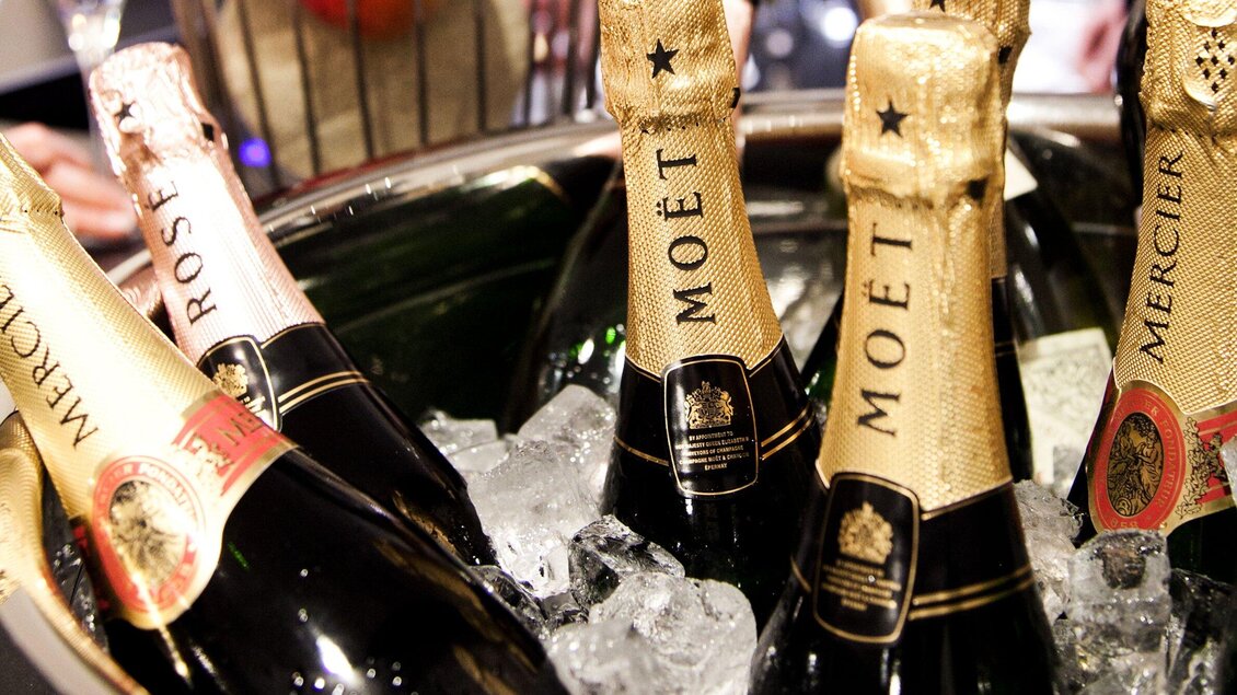 Eine Auswahl an Sektflaschen, die in einem Eiskübel liegen. Die Flaschen zeigen bekannte Marken wie Moët und Mercier. | © Tageskaffee Freiblick
