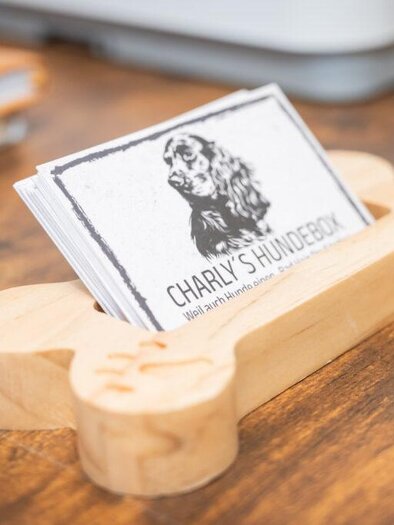 A creative stand in the shape of a dog bone holds business cards with the name "Charly's Dog Box." The background features a wood surface that creates a warm atmosphere. | © Tanja Noe