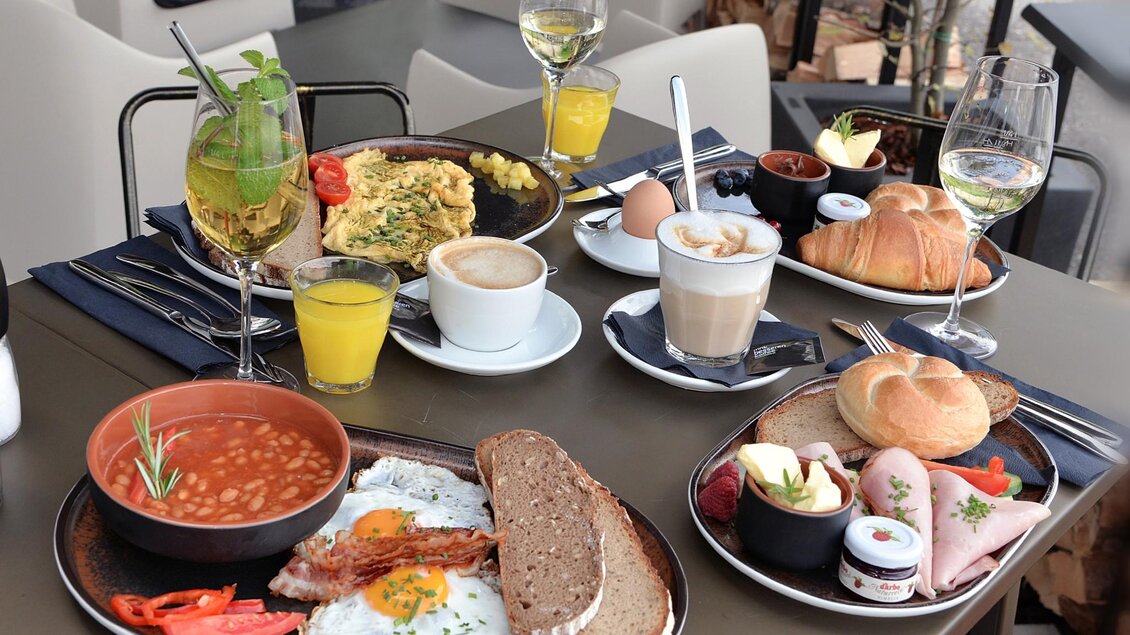 Ein reichhaltiges Frühstück mit Eiern, Speck, Bohnen, Brot und verschiedenen Beilagen. Dazu frische Getränke und süße Teilchen auf einem elegant gedeckten Tisch. | © Click Clack - Silvia Lambauer Fotografie