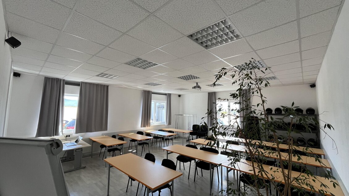 Ein heller Schulungsraum mit mehreren Tischen und Stühlen. Große Fenster lassen viel Tageslicht hinein, und eine Pflanze sorgt für eine angenehme Atmosphäre. | © Peter Hopf