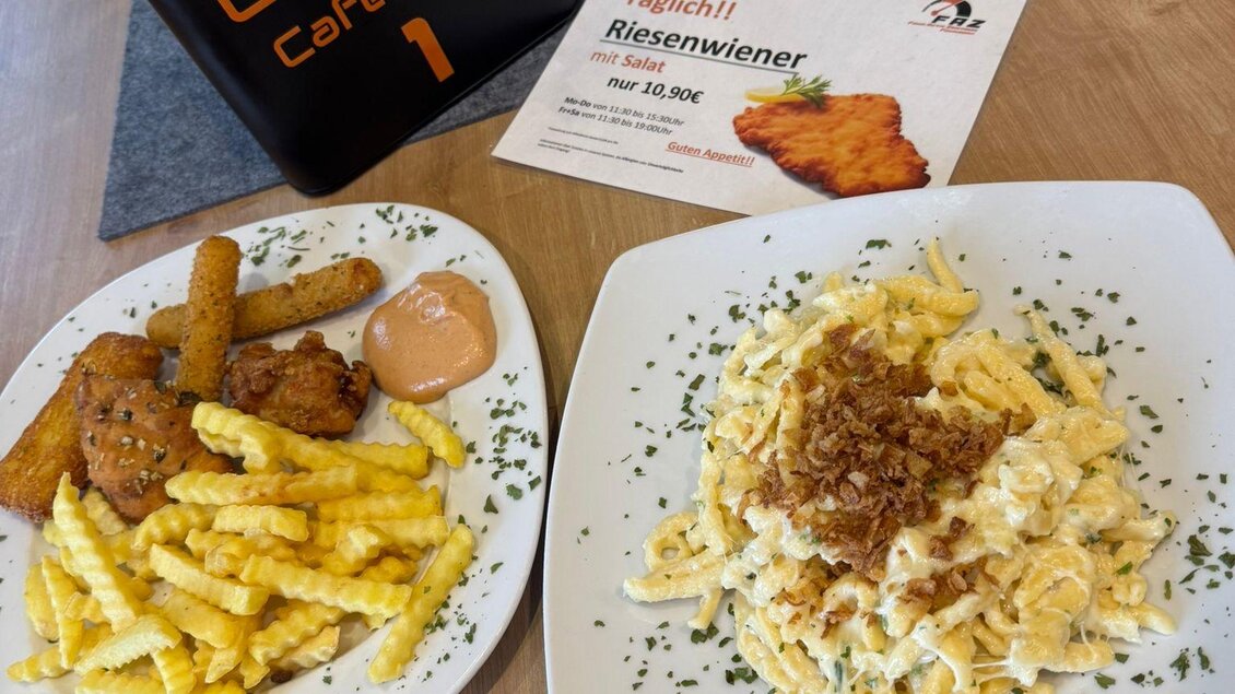 Ein Teller mit knusprigen Pommes, einem Fischgericht und einer Sauce auf der linken Seite. Auf der rechten Seite liegt ein Gericht mit Nudeln, Zwiebeln und einer würzigen Beilage. | © Peter Hopf