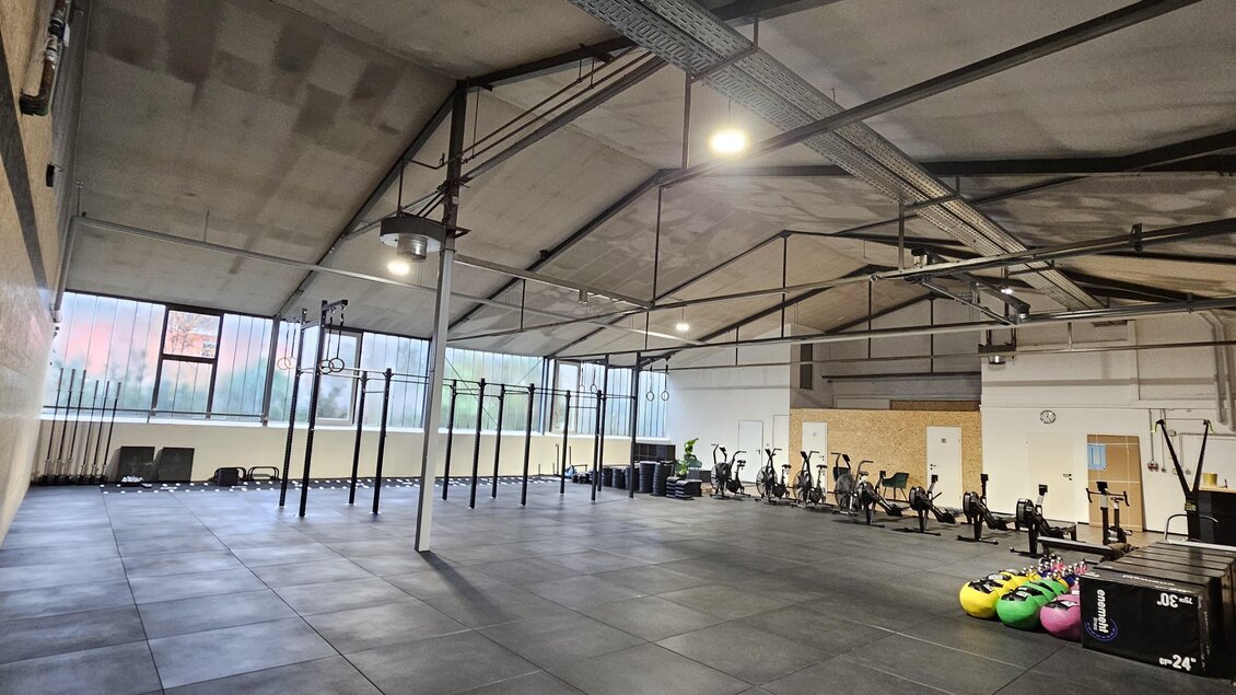 Ein großes, modernes Fitnessstudio mit offenen Räumen und hoher Decke. Verschiedene Trainingsgeräte stehen bereit, darunter Rudergeräte und Gewichte. | © Laura Reich