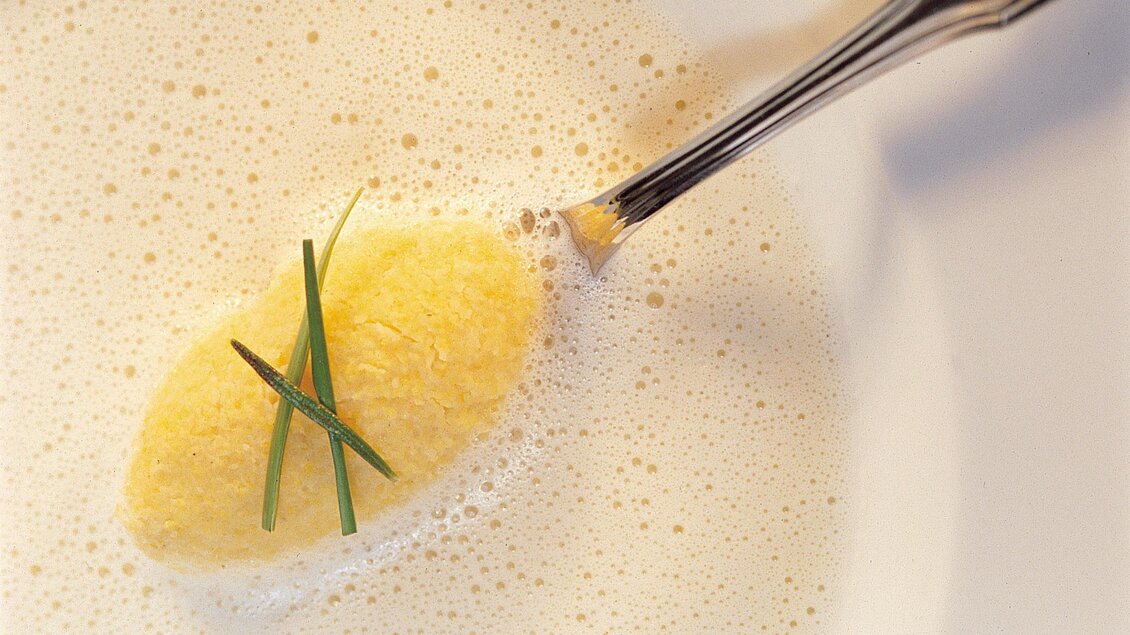 Ein elegantes Gericht mit einer kleinen, gelben Speise in einer sahnigen Suppe. Obenauf liegen ein paar feine Kräuter. | © Das Kappel