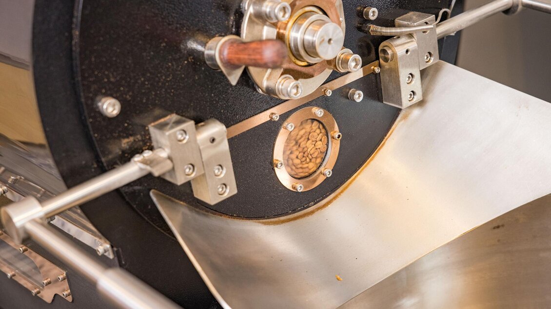 Eine Kaffeeröstmaschine mit metallischen Komponenten und einem glänzenden Edelstahlblech. Sie zeigt die präzise Technik des Röstprozesses. | © Wild und Team Fotoagentur GmbH
