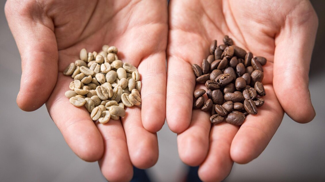 Zwei Hände halten Kaffeebohnen. Auf der linken Seite sind rohe, grüne Bohnen und auf der rechten Seite geröstete, braune Bohnen zu sehen. | © Wild und Team Fotoagentur GmbH