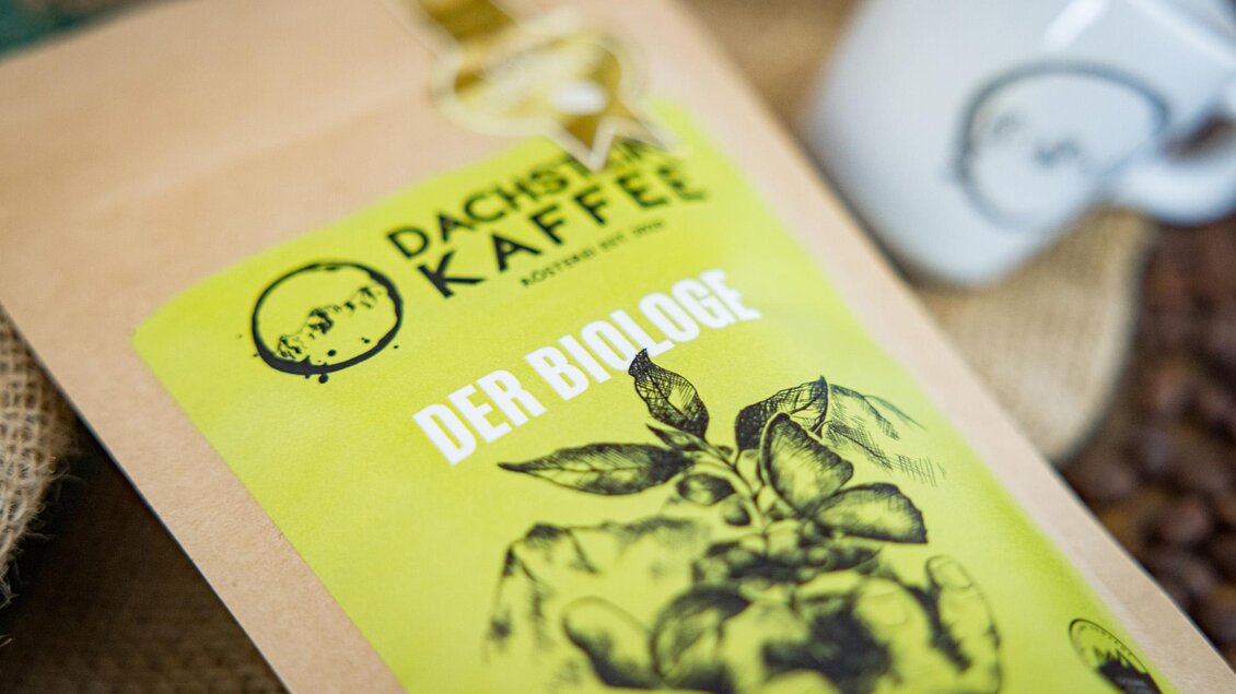 Eine Verpackung für Dachsberg Kaffee mit der Aufschrift "DER BIOLOGE". Im Hintergrund sind Kaffeebohnen und eine Tasse zu sehen. | © Wild und Team Fotoagentur GmbH
