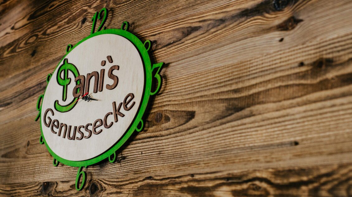 Ein Holzschild mit dem Schriftzug "Dani's Genussecke". Das Schild hat grüne und weiße Farben und ist an einer rustikalen Wand angebracht. | © TV Region Graz - Mias Photoart
