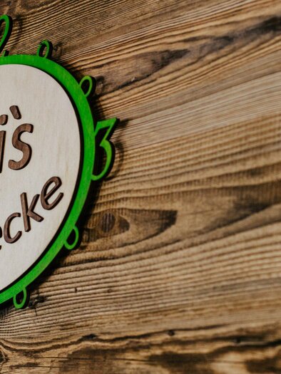 Ein Holzschild mit dem Schriftzug "Dani's Genussecke". Das Schild hat grüne und weiße Farben und ist an einer rustikalen Wand angebracht. | © TV Region Graz - Mias Photoart