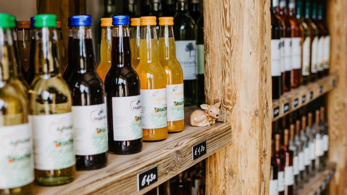 Eine Reihe von Flaschen mit verschiedenen Getränken steht auf einem Holzregal. Darunter befindet sich eine kleine Dekoration in Form eines Hasen. | © TV Region Graz - Mias Photoart