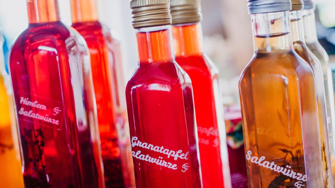 Bunte Flaschen mit verschiedenen Salatdressings stehen auf einem Tisch. Die Etiketten zeigen unterschiedliche Sorten, darunter Granatapfel. | © TV Region Graz - Mias Photoart