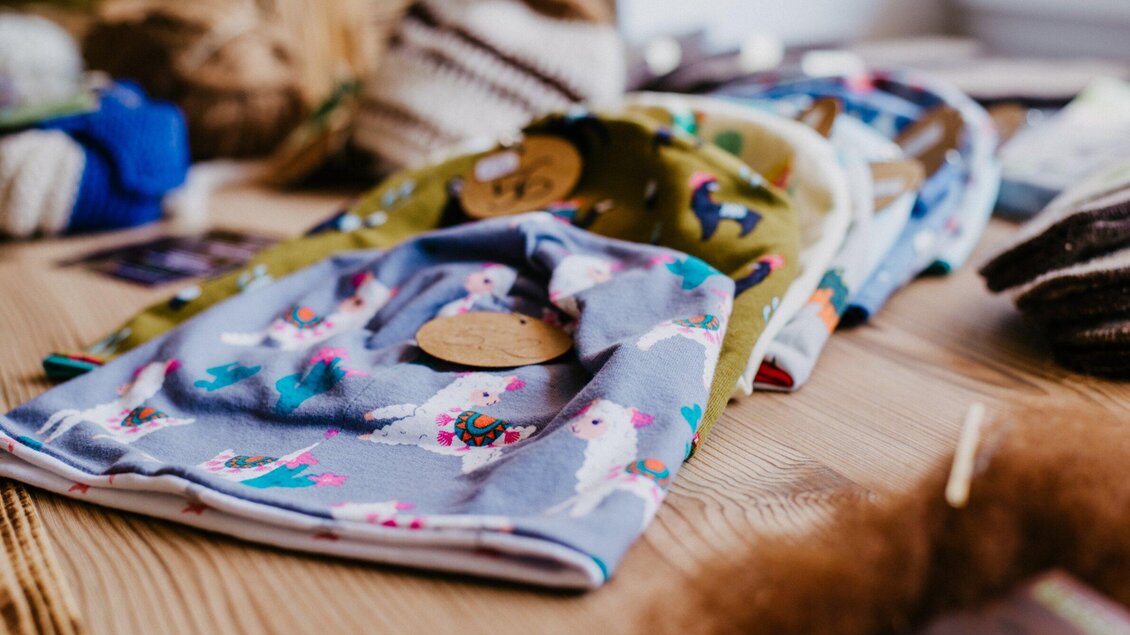 Bunte Stoffmützen liegen auf einem Holztisch. Die Mützen sind mit verschiedenen Mustern und Anhängern dekoriert. | © TV Region Graz - Mias Photoart