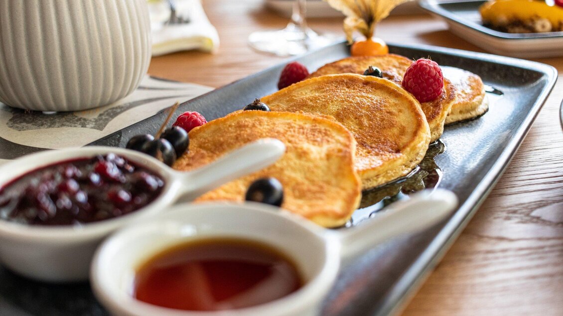 Ein Teller mit frisch gebackenen Pancakes, garniert mit Himbeeren und Heidelbeeren. Dazu gibt es zwei kleine Schalen mit Sirup und Marmelade. | © Das Franz