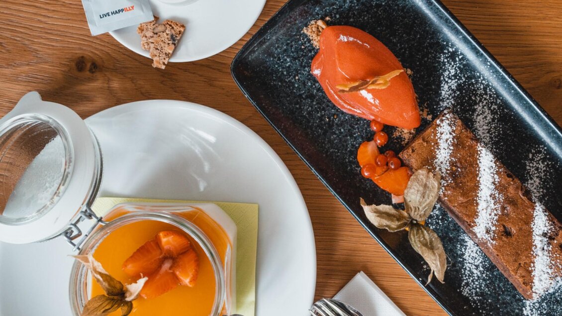 Ein Dessertteller mit Sorbet, Kuchen, Früchten und süßem Topping, daneben ein Glas Cappuccino. | © Das Franz