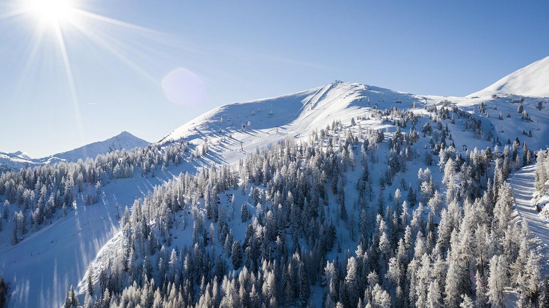 Eine schneebedeckte Berglandschaft unter einem klaren blauen Himmel. Die Sonne strahlt und wirft Schatten auf die verschneiten Bäume. | © Lukas Eisl