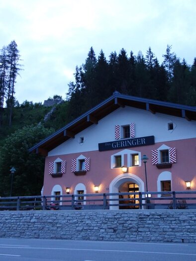 A cozy house with a pink facade and wooden cladding in the mountains. Surrounded by trees and a quiet street. | © Gasthof Geringer