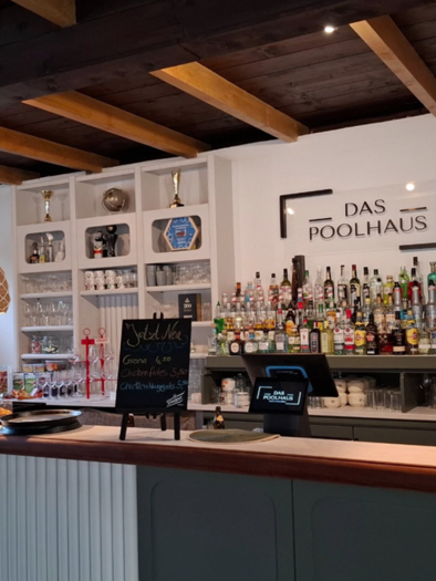 A stylish bar interior with a long counter and a variety of drinks in the background. The lighting is warm and inviting, with decorative lamps above the counter. | © Dominik Wolf