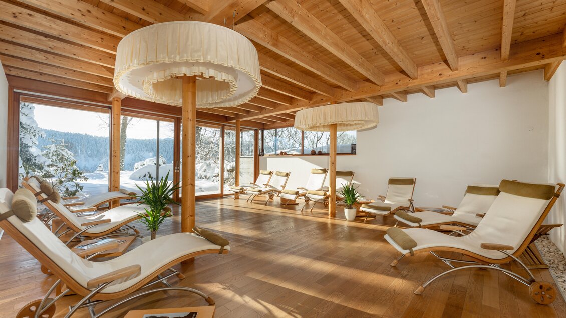 Ein heller Entspannungsraum mit bequemen Liegen und großen Fenstern, die einen Blick auf die winterliche Landschaft bieten. Die Holzdecke und die eleganten Lampen schaffen eine gemütliche Atmosphäre. | © Ramsauhof