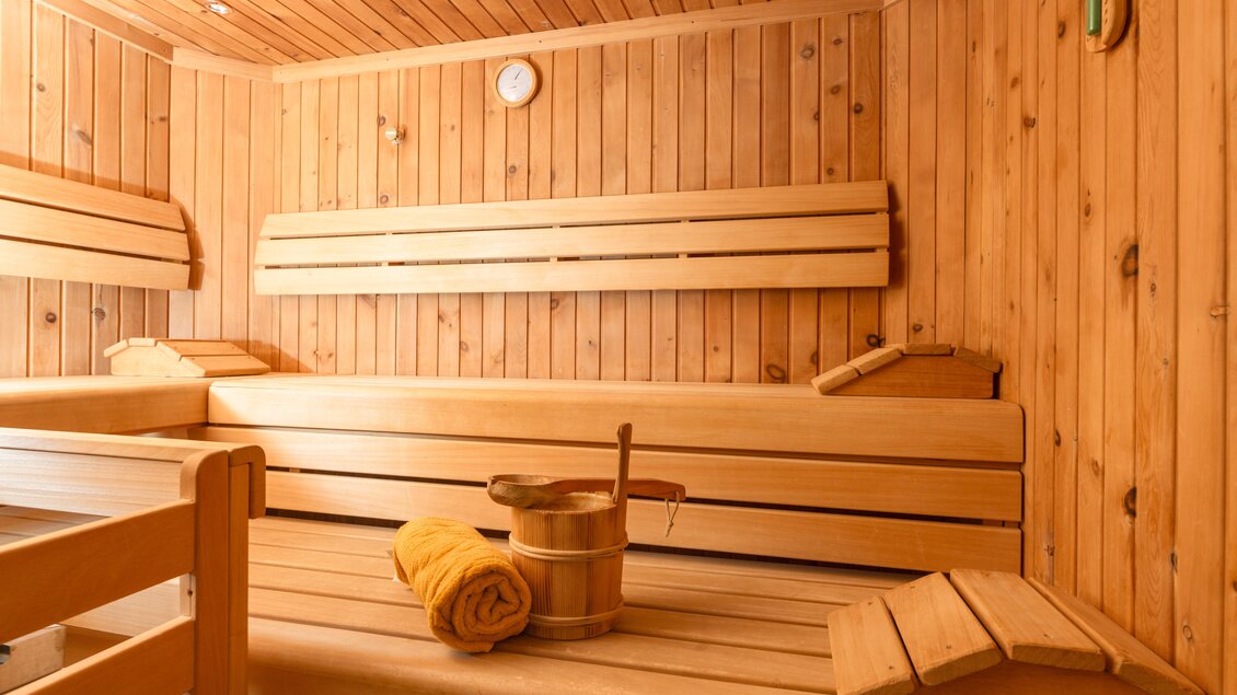 Eine gemütliche Sauna aus Holz mit Bänken und Zubehör. Im Vordergrund befindet sich ein Handtuch und ein Eimer. | © Ramsauhof