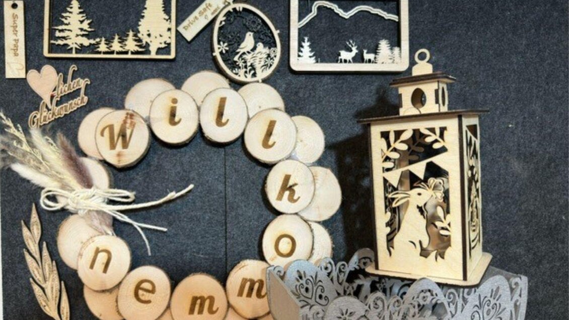 Ein rustikaler Dekorationskranz mit dem Wort "Willkommen" aus Holzscheiben. Neben dem Kranz befinden sich dekorative Holzfiguren und eine kleine Laterne. | © Angelika Mikula-Hubacek