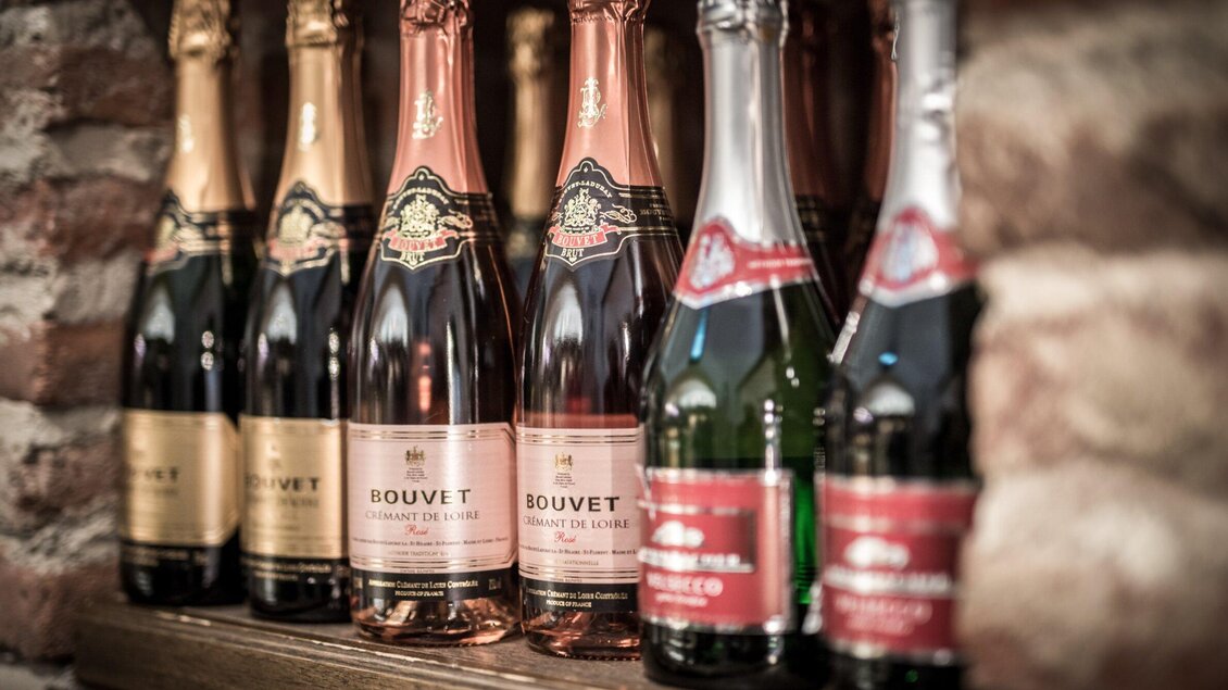 Eine Auswahl an Flaschen Sekt steht auf einem Regal. Die Flaschen haben verschiedene Etiketten und Farben. | © Delikatessen Nussbaumer