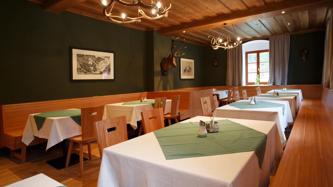 Ein gemütliches Restaurant mit Holztischen und -stühlen. Die Tische sind mit weißen Tischdecken und grünen Platzsets dekoriert.