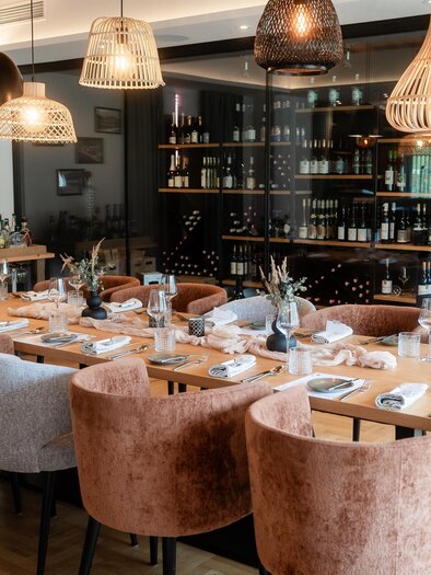 An elegant dining area with upholstered chairs and a long wooden table. The decor is modern and tasteful, complemented by stylish lamps. | © Der Literwirt