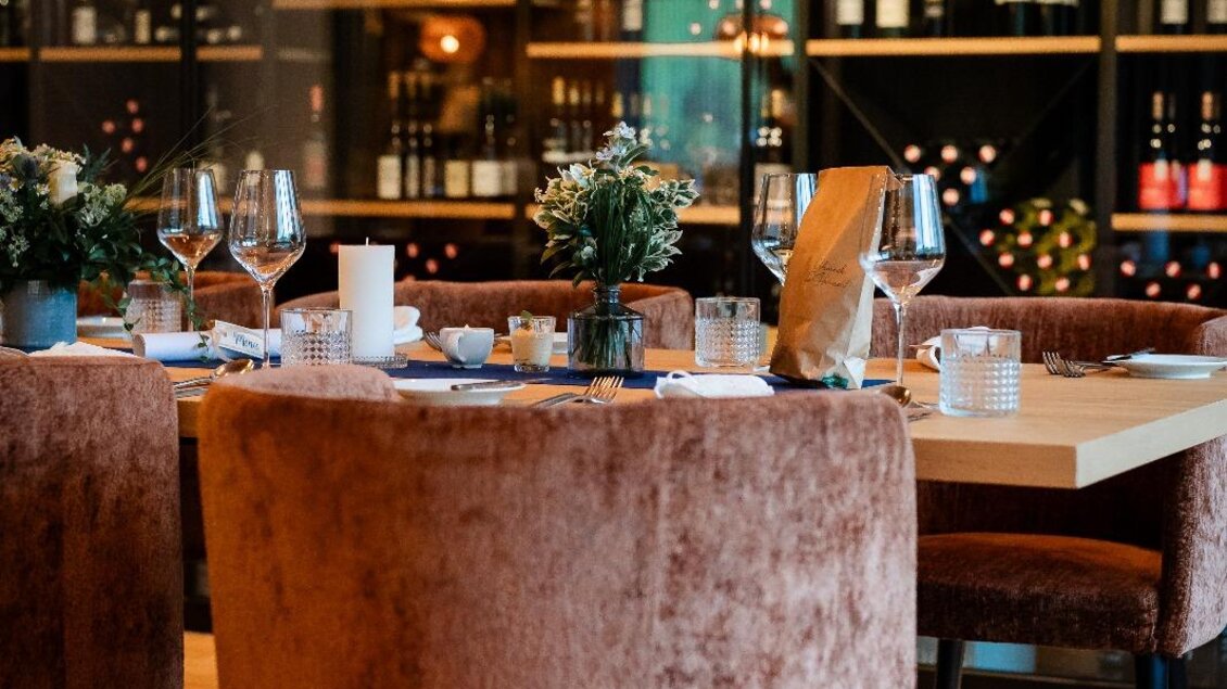 Ein stilvolles Restaurant mit eleganten, gepolsterten Stühlen und einem Tisch, der festlich gedeckt ist. Im Hintergrund sind Regale mit Weinflaschen sichtbar. | © Der Literwirt