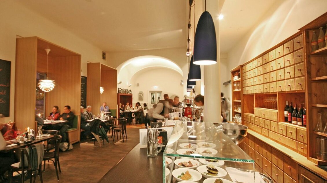 Blick ins Gasthaus mit Tischen, Weinschrank und Essen in der Vitrine, gemütliches Ambiente. | © Weitzer