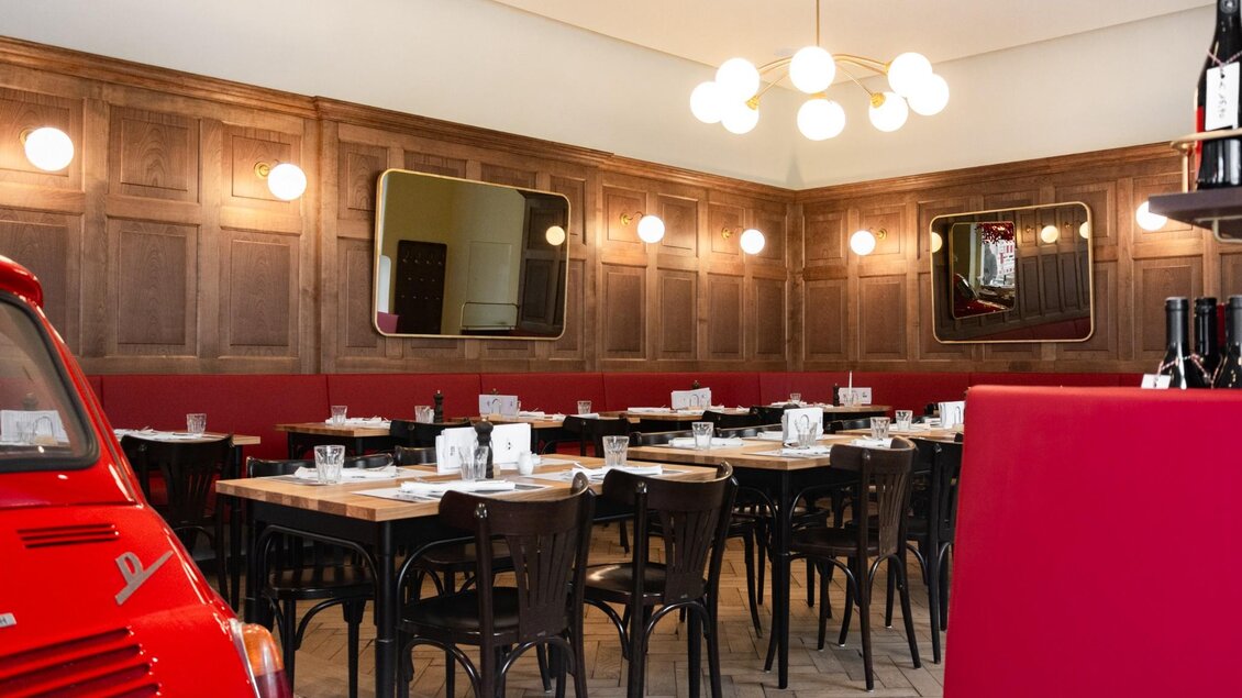  Innenansicht eines stilvollen Restaurants mit roten Sitzbänken, Holzwänden und einem Fiat 500 als Deko. | © Weitzer