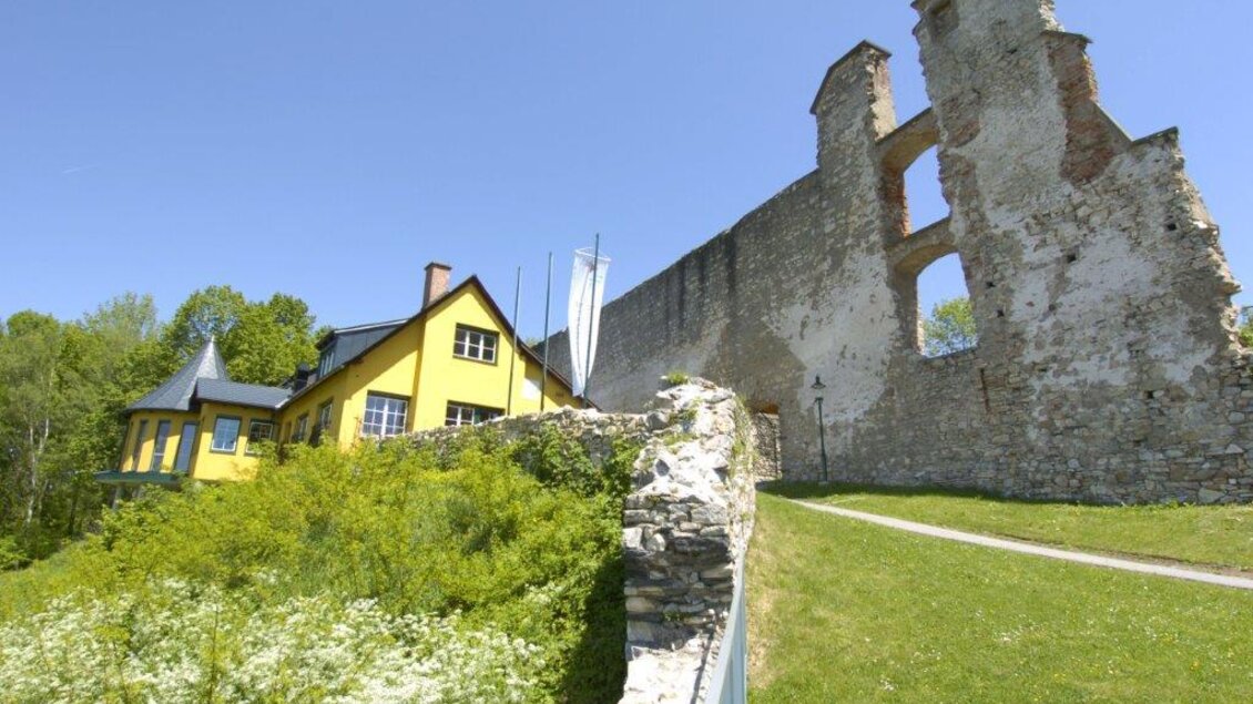 Ein historisches Schlossruine neben einem großen grünen Hügel. Im Vordergrund steht ein gelbes Haus mit einer klaren blauen Himmel im Hintergrund. | © Gerhard Langusch
