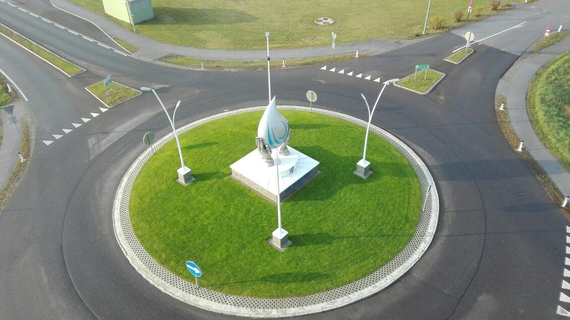 Ein Kreisverkehr mit einer Statue in der Mitte und grünem Rasen. Die Straßen sind gut markiert und mehrere Wege führen vom Kreisverkehr ab. | © Georg Strempfl