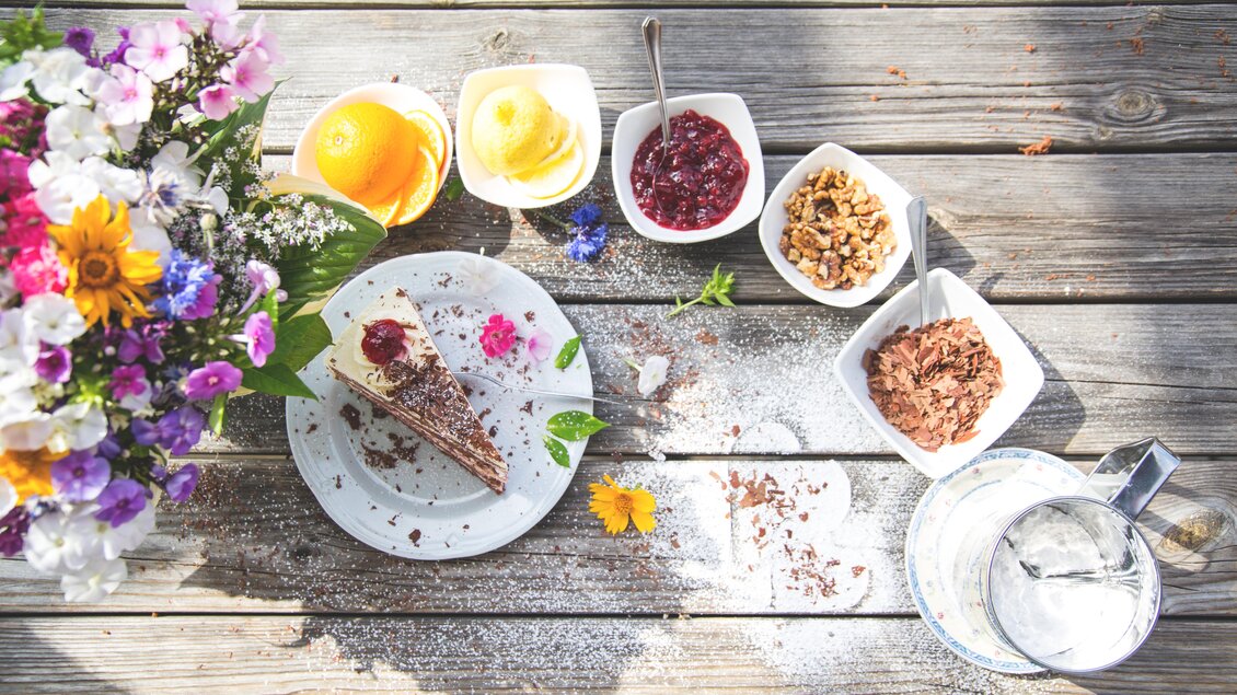Ein schöner Tisch mit einer leckeren Torte und verschiedenen Beilagen wie Marmelade, Müsli und frischen Früchten. Dazu steht eine bunte Blumenvase und ein Glas Wasser. | © Andreas Eder