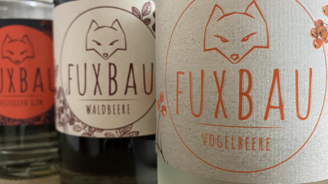 Drei Flaschen mit dem Label "Fuxbau" in verschiedenen Geschmacksrichtungen: Waldbeere und Vogelbeere. Die Etiketten zeigen ein stilisiertes Fuchs-Motiv. | © Lisa Polster