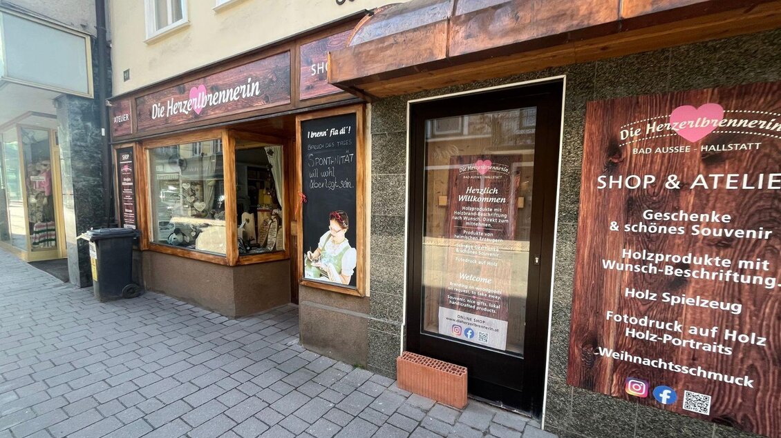 Ein Holzhandwerksladen mit Schaufenster, der Geschenke und Souvenirs anbietet. Die Fassaden sind mit einladenden Plakaten und Auslagen dekoriert. | © TVB Ausseerland Salzkammergut_Nathalie Schickinger
