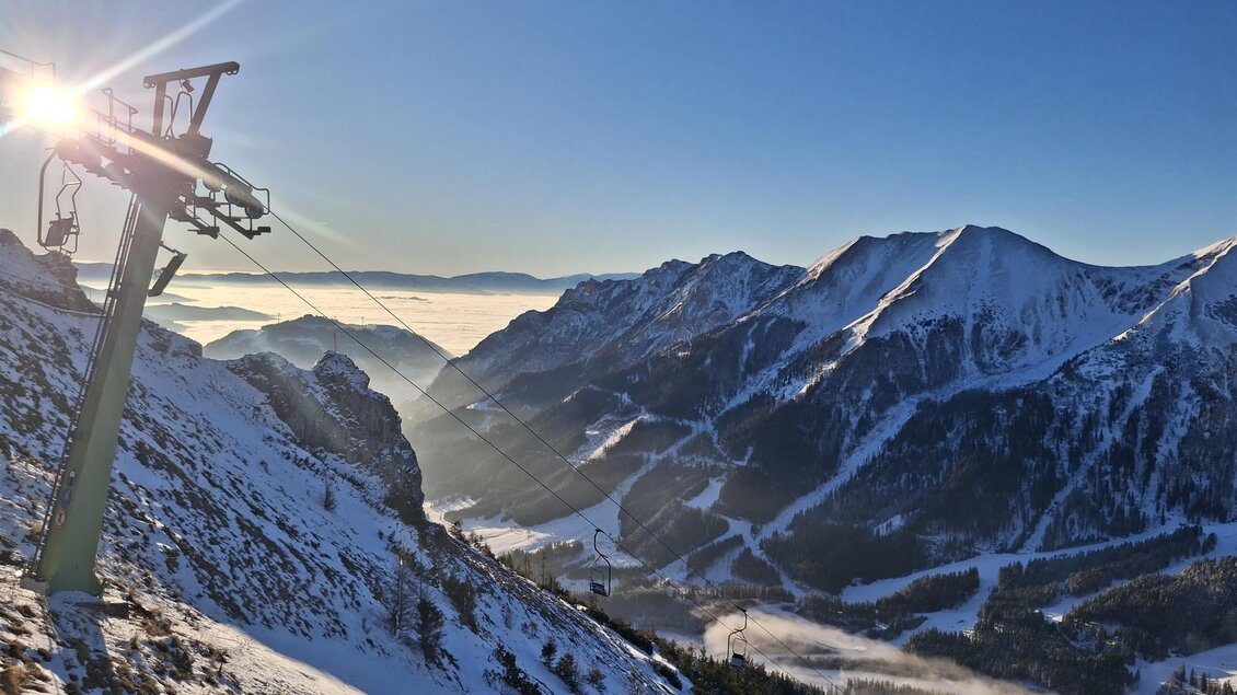 Eine beeindruckende Berglandschaft mit schneebedeckten Gipfeln und klaren Himmel. Im Vordergrund steht ein Skilift, der in die Höhe führt. | © Die Polsterei