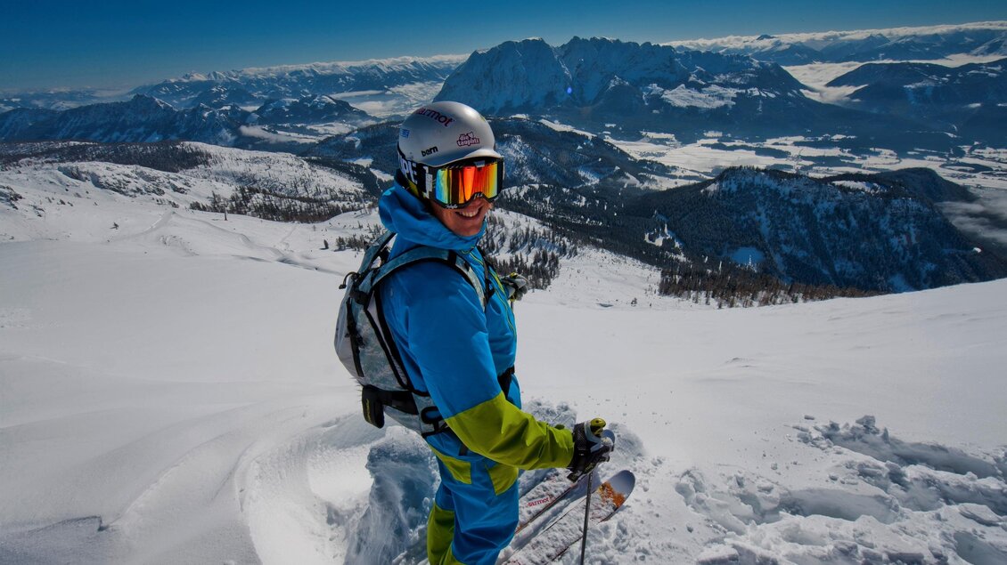 Ein Skifahrer steht auf einem verschneiten Berg mit beeindruckender Aussicht. Der Himmel ist klar und die Landschaft ist von Bergen umgeben. | © Die Tauplitz