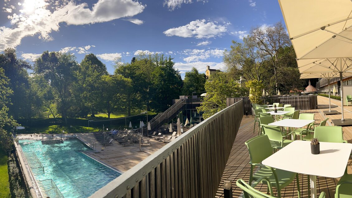 Ein entspannter Außenbereich mit einem Pool und grünen Stühlen. Der Himmel ist klar und die Landschaft ist von Bäumen umgeben. | © Die Therme der Ruhe Bad Gleichenberg