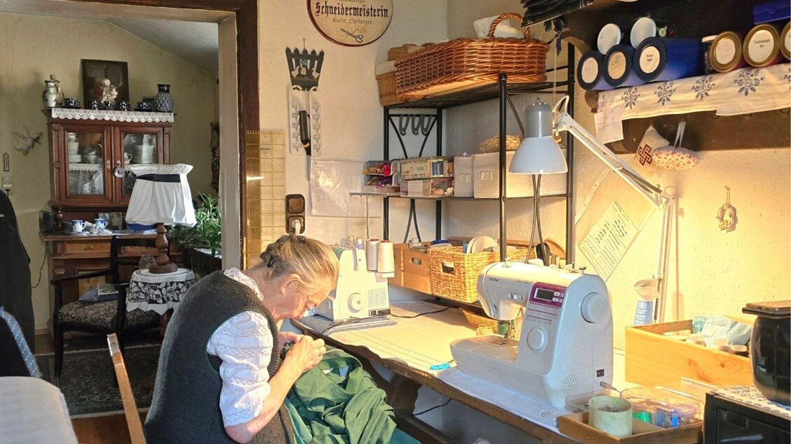 Ein gemütlicher Raum mit einer Näherin, die an einer Nähmaschine arbeitet. Auf dem Tisch sind Nähmaterialien und Werkzeuge ordentlich arrangiert. | © Stephanie Bor