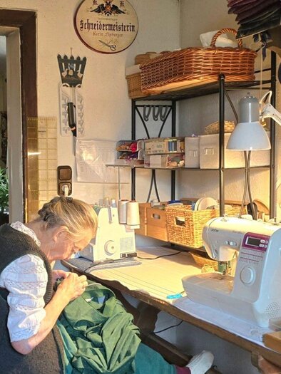 Ein gemütlicher Raum mit einer Näherin, die an einer Nähmaschine arbeitet. Auf dem Tisch sind Nähmaterialien und Werkzeuge ordentlich arrangiert. | © Stephanie Bor