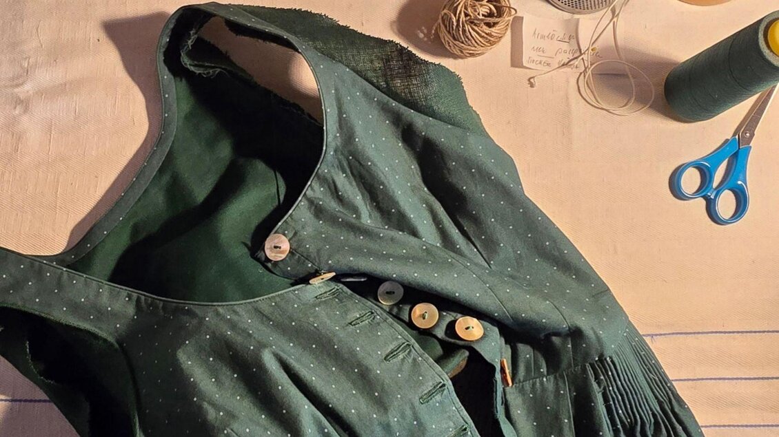 Ein grünes Kleid mit weißen Punkten liegt auf einem Tisch. Neben dem Kleid sind Nähutensilien wie Faden, Knöpfe und Scheren zu sehen. | © Stephanie Bor