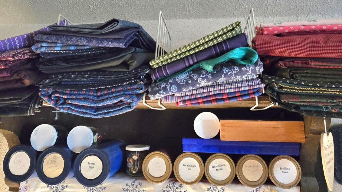 Eine Sammlung von bunten Stoffen, ordentlich gestapelt auf Regalen. Darunter befinden sich verschiedene Behälter mit beschrifteten Inhalten. | ©  Stephanie Bor
