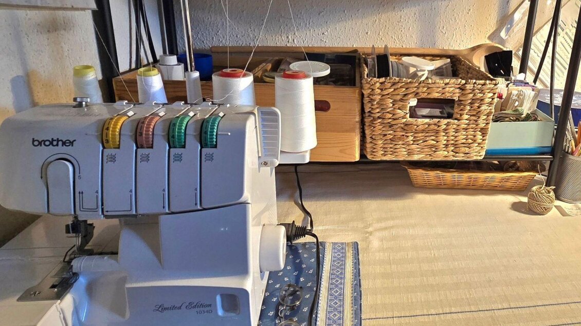 Eine Nähmaschine steht auf einem Tisch, umgeben von verschiedenen Materialien und Zubehör. Im Hintergrund sind Körbe mit weiteren Utensilien zu sehen. | ©  Stephanie Bor